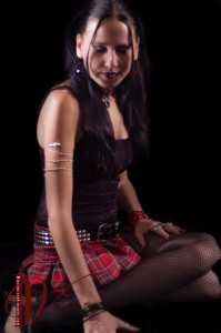 Jade in contemplative pose wearing plaid skirt and goth style mesh blouse.